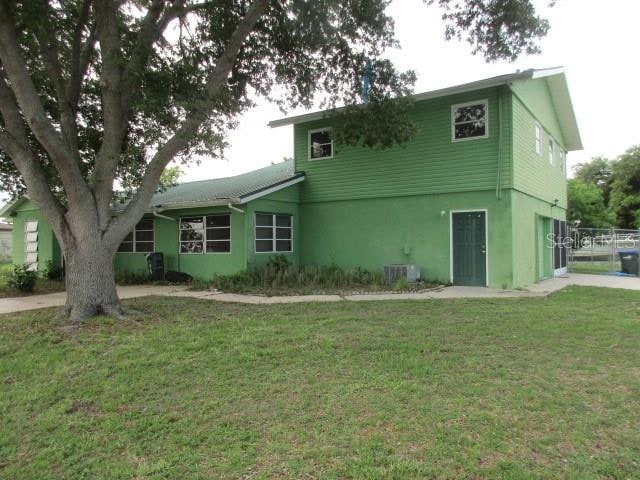 rear view of house with central air condition unit and a lawn