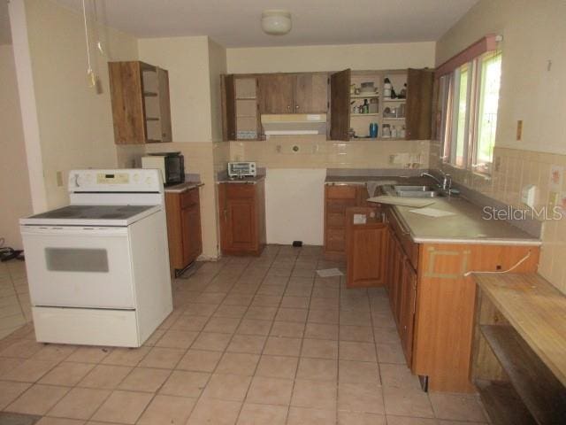 kitchen featuring sink, kitchen peninsula, light tile patterned floors, decorative backsplash, and white electric range