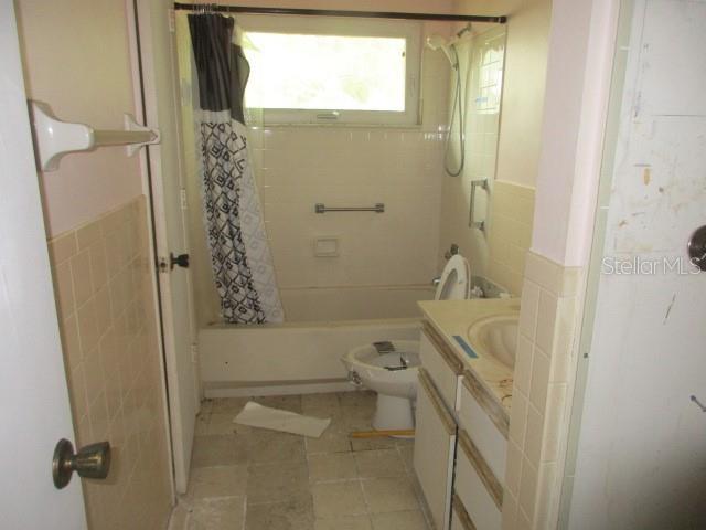 full bathroom with tile patterned flooring, shower / bathtub combination with curtain, toilet, vanity, and tile walls