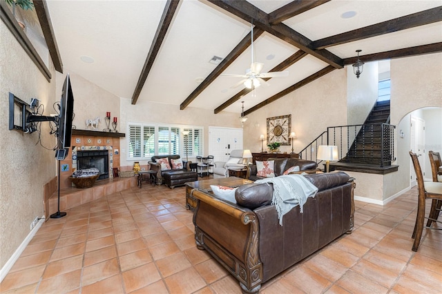 tiled living room with a fireplace, high vaulted ceiling, beam ceiling, and ceiling fan