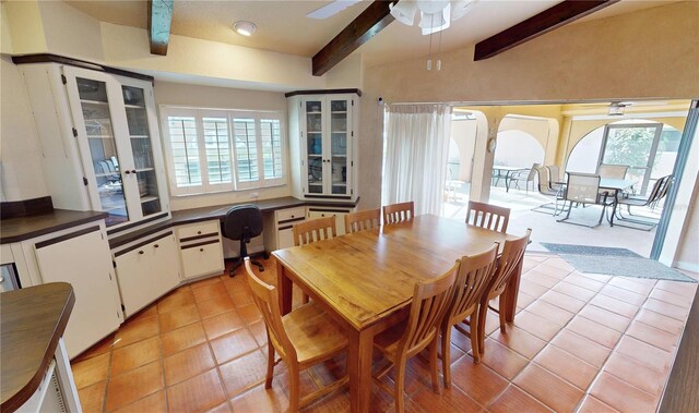 tiled dining area with beamed ceiling, built in desk, and ceiling fan