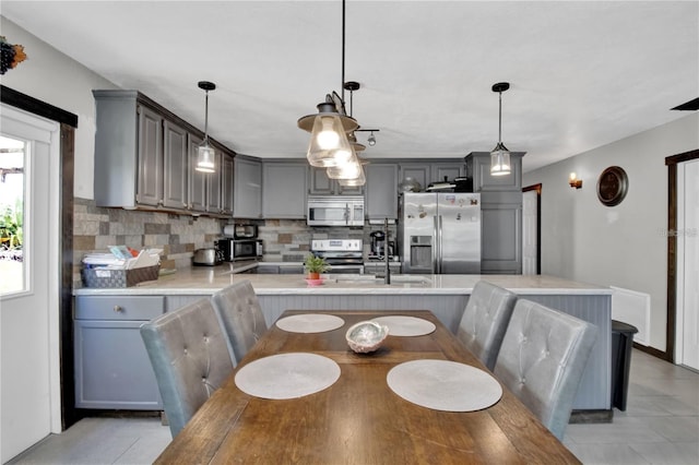 kitchen with gray cabinets, light countertops, decorative backsplash, appliances with stainless steel finishes, and a kitchen bar