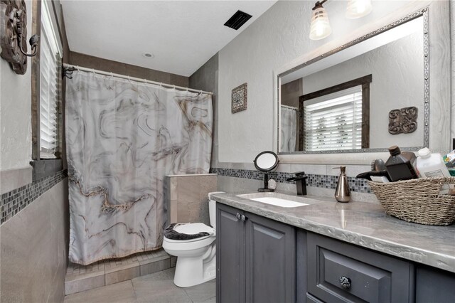 bathroom with backsplash, toilet, vanity, tile walls, and tile patterned floors