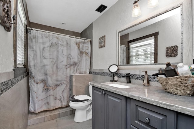 bathroom featuring a textured wall, toilet, tile patterned floors, vanity, and tile walls