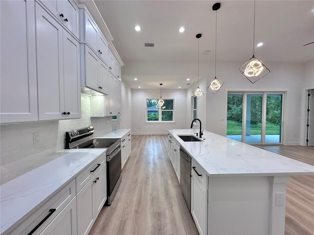 kitchen with appliances with stainless steel finishes, light stone countertops, pendant lighting, sink, and a spacious island