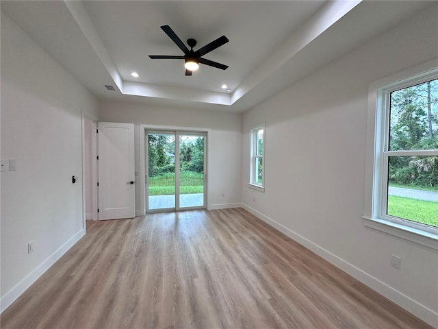 unfurnished room with a wealth of natural light, a tray ceiling, ceiling fan, and light wood-type flooring