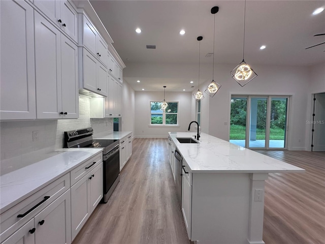 kitchen with pendant lighting, light stone countertops, an island with sink, stainless steel electric stove, and light wood-type flooring