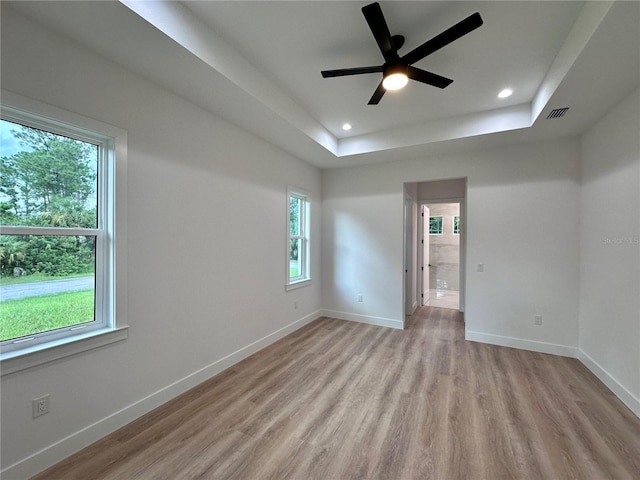 unfurnished room featuring a healthy amount of sunlight, a tray ceiling, ceiling fan, and light hardwood / wood-style flooring