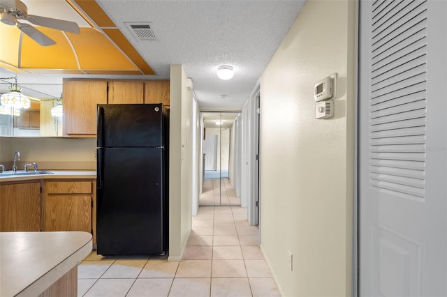 kitchen with sink, black refrigerator, light tile patterned flooring, ceiling fan, and a textured ceiling