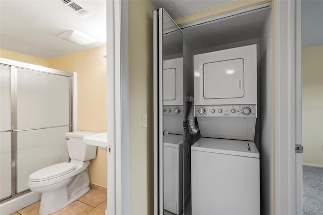 clothes washing area featuring a textured ceiling, light tile patterned floors, and stacked washer / dryer