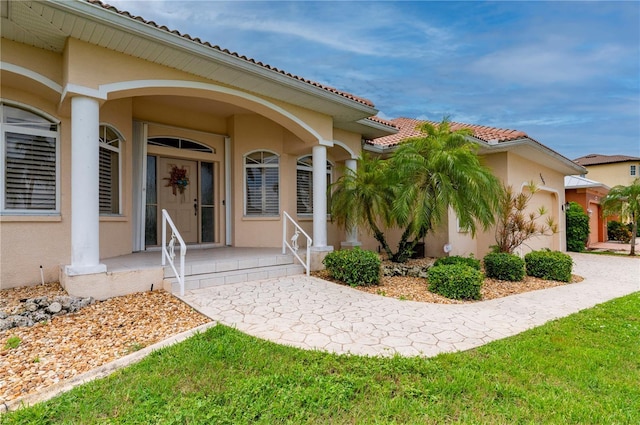 view of exterior entry featuring covered porch, a tiled roof, a lawn, and stucco siding