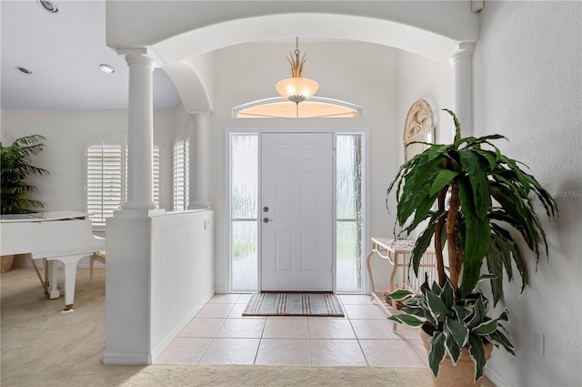 foyer entrance featuring light carpet, decorative columns, baseboards, and light tile patterned floors