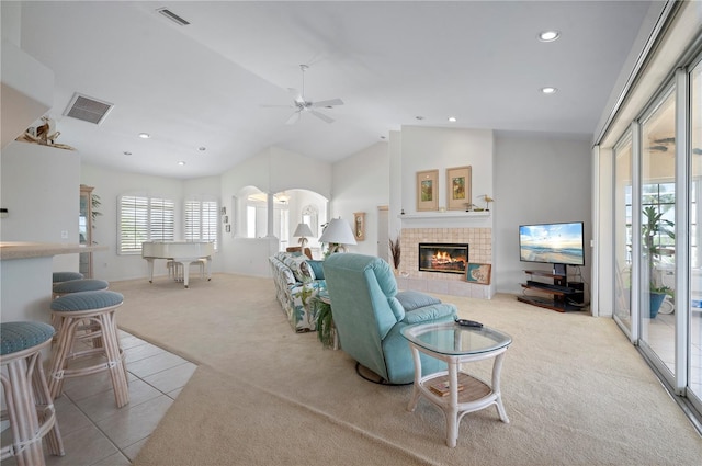 living room with ceiling fan, lofted ceiling, a tiled fireplace, and light carpet