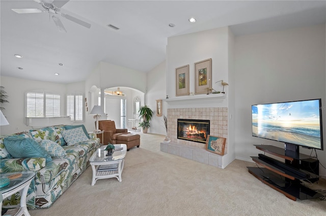 living room featuring a tiled fireplace, ceiling fan, and light colored carpet