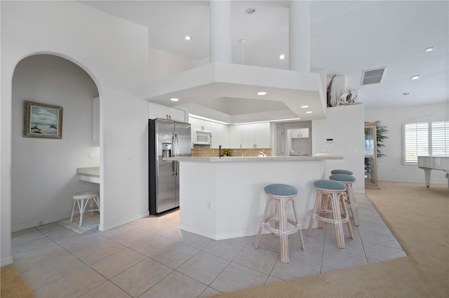 kitchen with tasteful backsplash, white cabinets, a kitchen bar, stainless steel refrigerator with ice dispenser, and light carpet