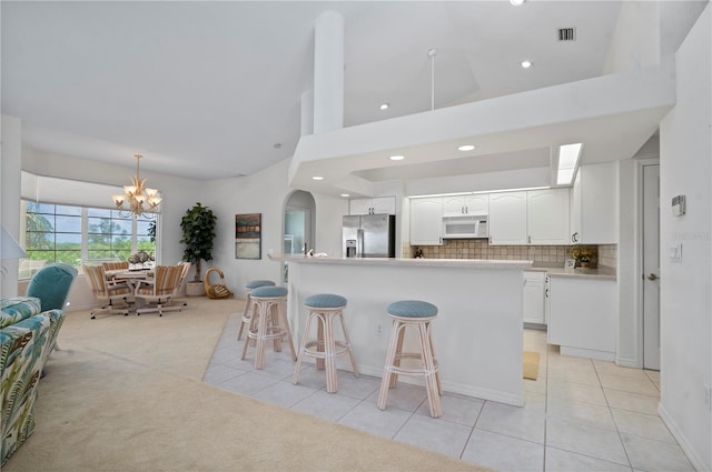 kitchen featuring white cabinets, stainless steel fridge with ice dispenser, a breakfast bar, light carpet, and a notable chandelier