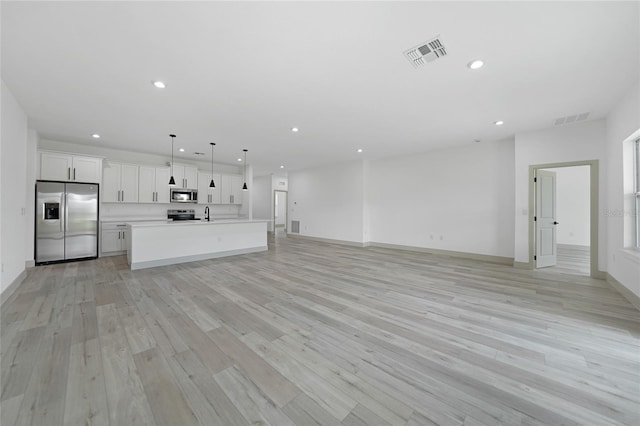 kitchen featuring white cabinets, hanging light fixtures, light wood-type flooring, an island with sink, and appliances with stainless steel finishes