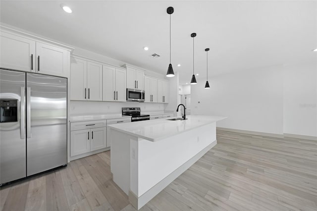 kitchen with stainless steel appliances, sink, a center island with sink, white cabinets, and hanging light fixtures