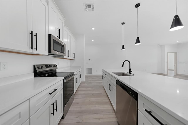 kitchen with appliances with stainless steel finishes, sink, light hardwood / wood-style floors, white cabinetry, and hanging light fixtures