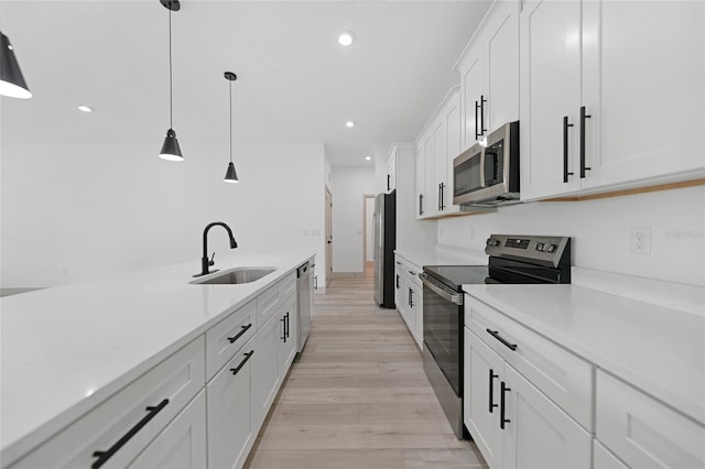 kitchen with sink, appliances with stainless steel finishes, decorative light fixtures, white cabinets, and light wood-type flooring