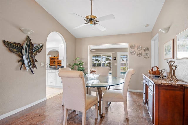 dining area featuring ceiling fan, arched walkways, tile patterned flooring, baseboards, and vaulted ceiling