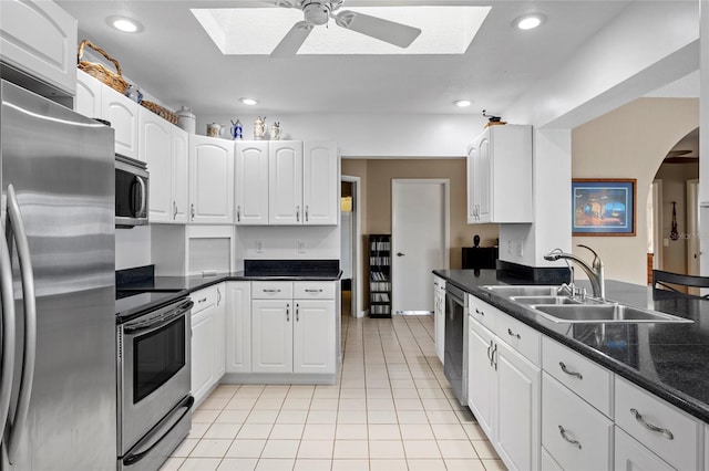 kitchen featuring arched walkways, light tile patterned floors, stainless steel appliances, a sink, and white cabinets