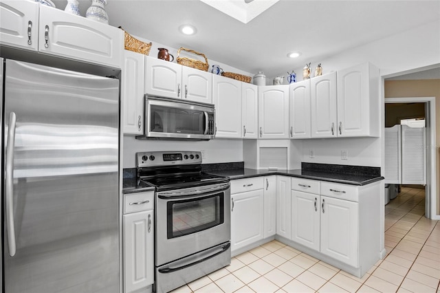 kitchen with light tile patterned floors, stainless steel appliances, dark countertops, and white cabinetry