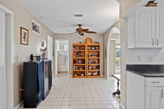 kitchen featuring arched walkways, light tile patterned floors, a textured ceiling, visible vents, and dark countertops