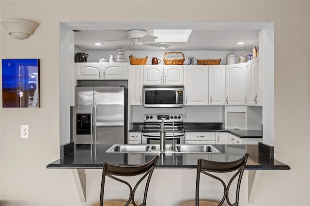 kitchen featuring ceiling fan, stainless steel appliances, a peninsula, white cabinetry, and a kitchen breakfast bar