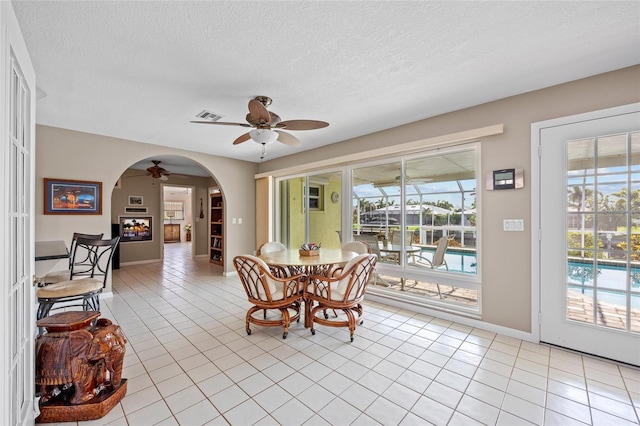 dining room with light tile patterned floors, visible vents, arched walkways, and ceiling fan