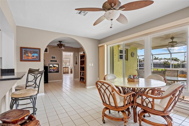 dining space featuring arched walkways, a textured ceiling, light tile patterned flooring, visible vents, and baseboards