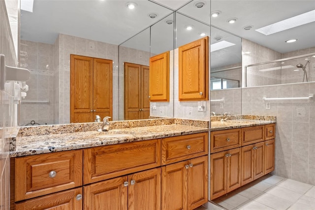 full bathroom featuring a skylight, tile walls, double vanity, a sink, and a shower stall