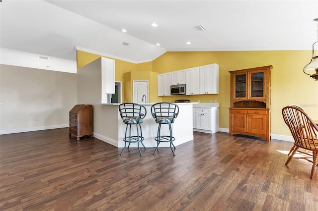 kitchen with vaulted ceiling, dark wood-type flooring, a breakfast bar area, and white cabinets