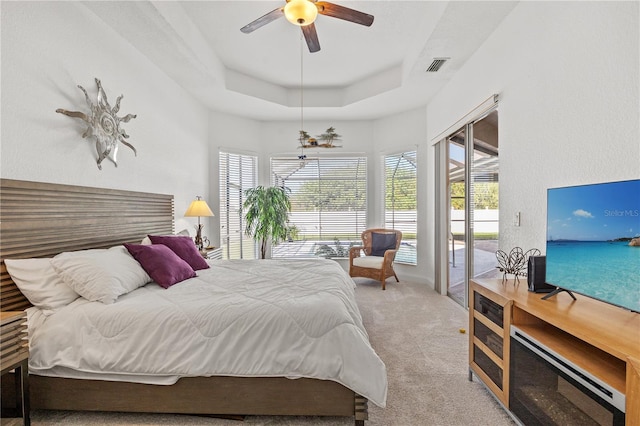 bedroom featuring a tray ceiling, light carpet, access to outside, and ceiling fan