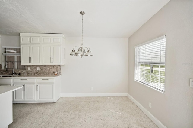 kitchen featuring tasteful backsplash, a notable chandelier, hanging light fixtures, white cabinetry, and sink