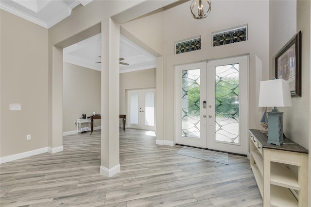 foyer entrance featuring ornamental molding, a towering ceiling, light wood-type flooring, and french doors