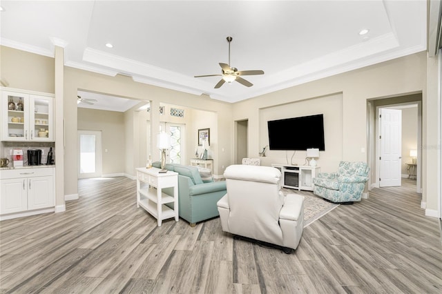 living room with a raised ceiling, ornamental molding, ceiling fan, and light hardwood / wood-style flooring