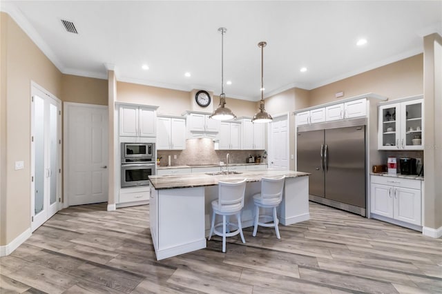 kitchen with hanging light fixtures, white cabinetry, a kitchen island with sink, and built in appliances