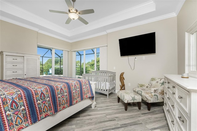 bedroom with light hardwood / wood-style flooring, ceiling fan, access to exterior, a tray ceiling, and ornamental molding