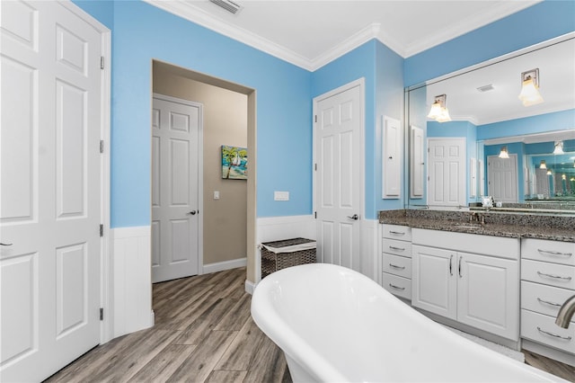 bathroom featuring vanity, wood-type flooring, ornamental molding, and a tub