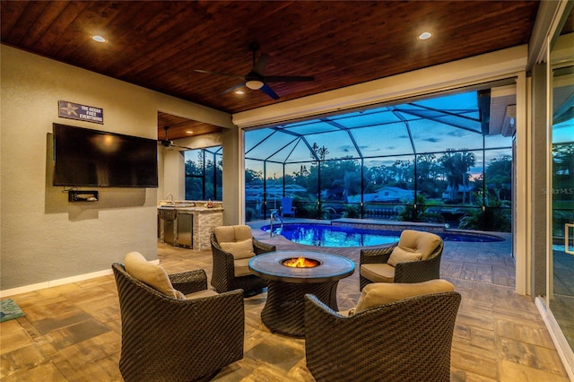 view of patio with an outdoor fire pit, glass enclosure, ceiling fan, and exterior kitchen