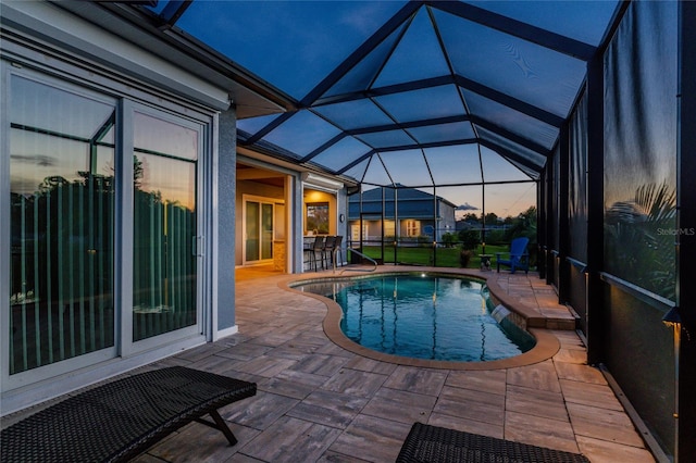 pool at dusk with a lanai, an outdoor bar, and a patio area