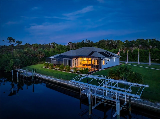 back house at dusk with a water view, a yard, and a lanai