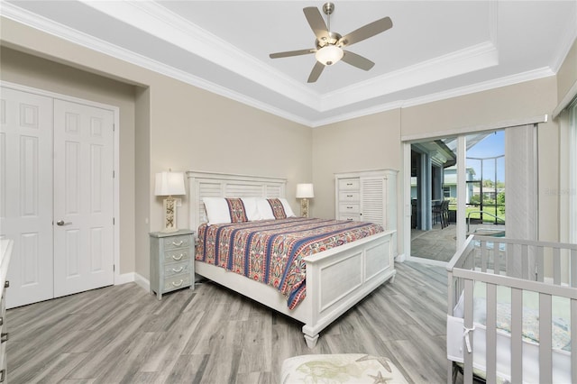 bedroom featuring ornamental molding, access to outside, light wood-type flooring, and a tray ceiling