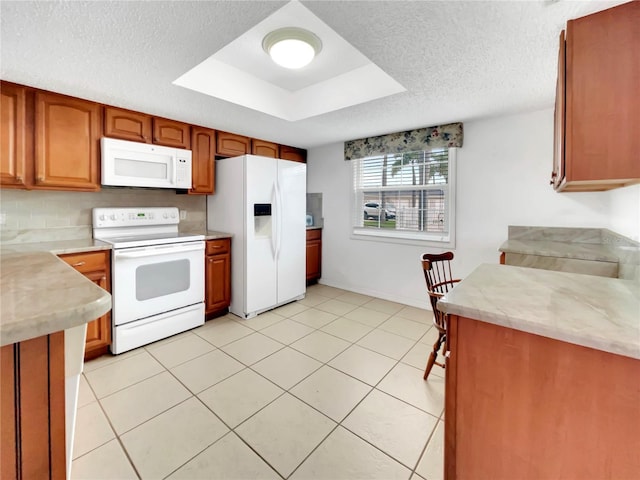 kitchen with a raised ceiling, white appliances, light tile patterned floors, and a textured ceiling