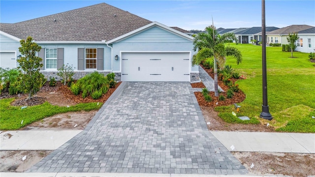 ranch-style house featuring an attached garage, stone siding, decorative driveway, stucco siding, and a front yard