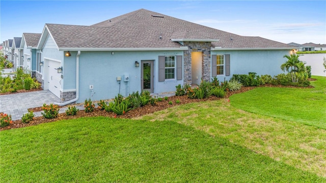 rear view of property with an attached garage, stucco siding, a shingled roof, and a yard