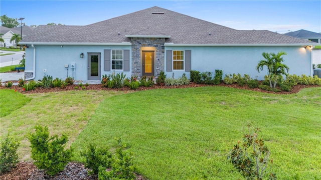 ranch-style home with stone siding, a front lawn, a shingled roof, and stucco siding