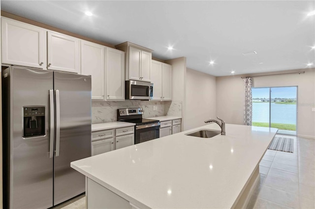 kitchen with a center island with sink, stainless steel appliances, tasteful backsplash, light countertops, and a sink