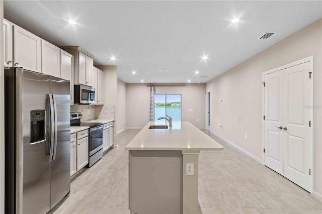 kitchen with stainless steel appliances, tasteful backsplash, visible vents, a sink, and an island with sink